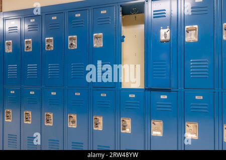 Armadietto singolo aperto vuoto in metallo blu lungo un corridoio non descrittivo in una tipica scuola superiore degli Stati Uniti. Foto Stock