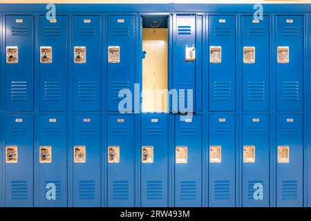 Armadietto singolo aperto vuoto in metallo blu lungo un corridoio non descrittivo in una tipica scuola superiore degli Stati Uniti. Foto Stock