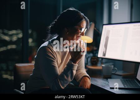 Donna professionale che lavora fino a tardi nel suo ufficio domestico, telefonando per discutere di un progetto con i suoi colleghi. Felice donna d'affari che mostra impegno Foto Stock