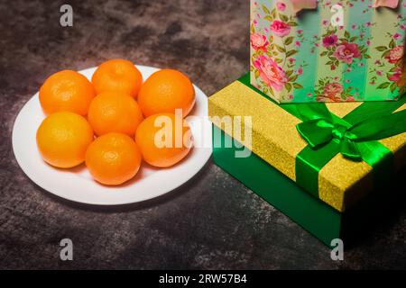 Un sacco di mandarini su un piatto bianco accanto ai regali di Capodanno, una bellissima confezione regalo con un nastro su sfondo grigio. Foto Stock