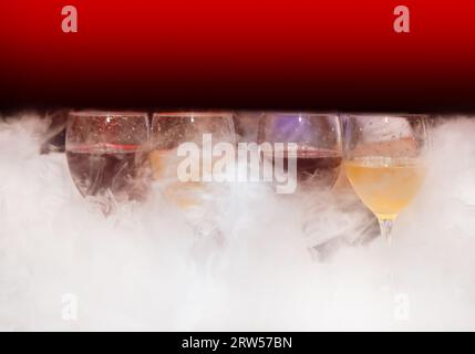 4 quattro bicchieri con bevande alcoliche colorate in fumo di narghilè bianco o fumo di ghiaccio liquido su uno sfondo astratto. Foto Stock