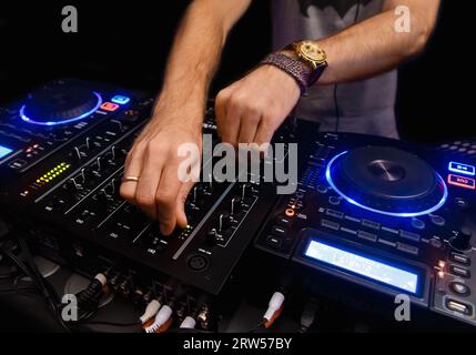 Le mani di un DJ professionista lavorano sul controller, sull'attrezzatura, sullo strumento per mixare e suonare la musica da club, sulla vita notturna. Foto Stock