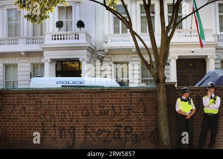 Prima della protesta, i graffiti realisti vengono spruzzati sul muro fuori dall'ambasciata iraniana mentre la polizia guarda i manifestanti che si riuniscono di fronte. La protesta segna il primo anniversario della morte di Mahsa Amini 22, che è stato arrestato dalla polizia della moralità in Iran dopo aver detto che indossava il suo hijab in modo errato. Amini e' stata portata in un centro di detenzione dove e' collassata ed e' morta. La sua morte e la morte di altri a seguito di una repressione in Iran hanno ispirato il movimento Women Life Freedom in tutto il mondo. I manifestanti chiedono la fine della Repubblica islamica. Foto Stock