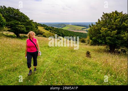 Una donna di mezza età cammina su un ripido prato di fiori selvatici fino a Bow Hill a Kingley vale, con viste mozzafiato sulla campagna del West Sussex, in Inghilterra. Foto Stock