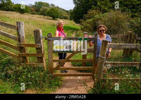Due donne di mezza età camminano attraverso un cancello di legno sulla strada fino alla cima di Bow Hill a Kingley vale, nel West Sussex, in Inghilterra. Foto Stock