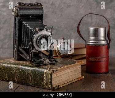 Macchina fotografica con soffietti antichi su un libro antico con un thermos di caffè e un orologio da tasca accanto Foto Stock