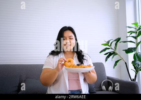 La donna Plus size sta mangiando la ciambella. Concetto di assistenza sanitaria e stile di vita. Foto Stock