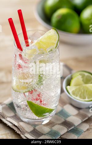 Bicchiere di acqua frizzante fredda con spicchi di lime su un tavolo di legno Foto Stock