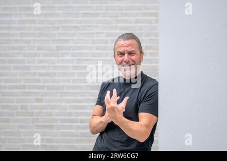 Uomo dai capelli grigi di mezza età con una barba grigia che guarda disperatamente nella fotocamera di fronte a un muro di mattoni bianchi Foto Stock