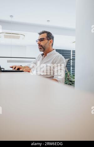 Uomo d'affari senior che ha una riunione online in ufficio, discutendo con il cliente. Uomo d'affari maturo che lavora sul computer portatile in un'officina moderna. Foto Stock