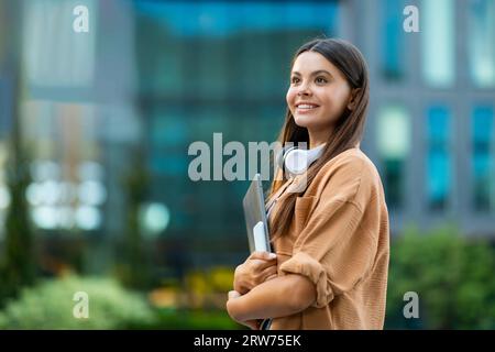 Felice bella studentessa in posa al campus universitario, con in mano gadget Foto Stock