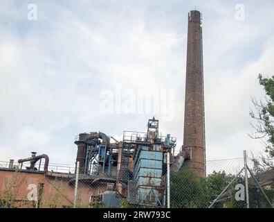 Un edificio abbandonato con un alto camino in mattoni contro il cielo. Area industriale di hälleforsnäs svezia Foto Stock