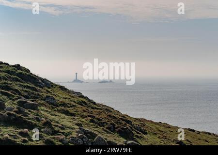 Costa frastagliata della Cornovaglia con un faro distante su un affioramento roccioso in un mare calmo Foto Stock