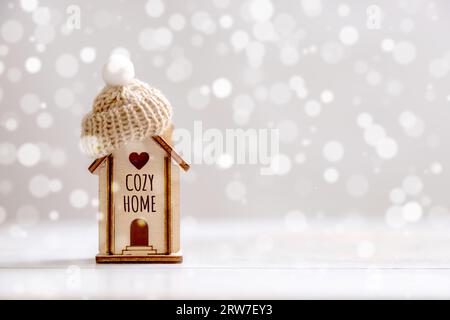 Una piccola casa con un cappello si erge su uno sfondo di legno. Il concetto di pagamento delle utenze, risparmio energetico, isolamento domestico, sistema di riscaldamento Foto Stock