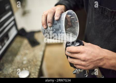 Mani di una giovane persona sconosciuta che versa vernice in un serbatoio di una pistola a spruzzo nella sua officina. Vista ravvicinata con spazio di copia. Foto Stock