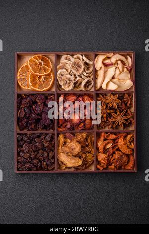 Variazione di frutta secca fragola, mela, ciliegia, banana, pesca, prugna e anice stellato in una scatola su uno sfondo di cemento scuro Foto Stock