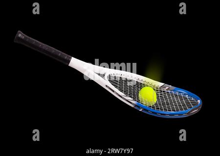 Broken tennis racquet with tennis ball going through the strings on a black background Foto Stock