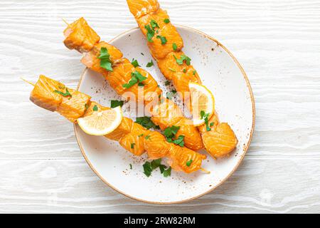 Spiedini di salmone alla griglia conditi con prezzemolo verde e limone su piatto di ceramica su tavola rustica in legno bianco vista dall'alto, salutare Foto Stock