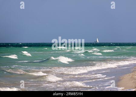 Spiaggia di mare vuota, vista delle onde e barca a vela in lontananza. Costa oceanica, sfondo per le vacanze Foto Stock