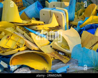 Vecchie sedie di plastica rotte allo stadio. Concetto di rivolta dei fan. Un mucchio di sedie di plastica. Rotto e abbandonato. Sedie gialle e blu Foto Stock