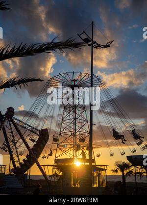 Batumi, Georgia. 09.10.2023 sagome di persone sulla giostra. Concetto di divertimento e intrattenimento. Persone su caroselli al tramonto. Città di villeggiatura. Lunap Foto Stock