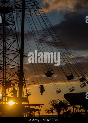 Sagome di persone sulla giostra. Concetto di divertimento e intrattenimento. Persone su caroselli al tramonto. Città di villeggiatura. Lunapark. Adrenalina. Speed carous Foto Stock