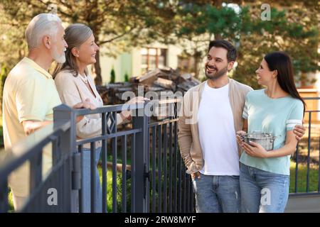 Rapporto amichevole con i vicini. Famiglia giovane che parla con coppie anziane vicino a recinzione all'aperto Foto Stock