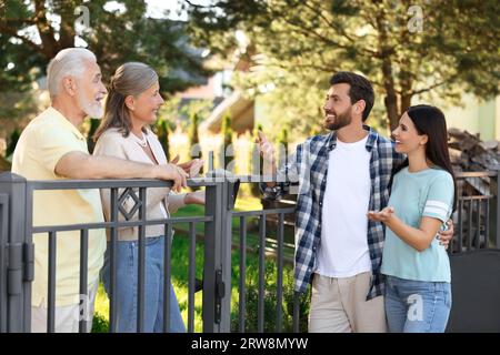 Rapporto amichevole con i vicini. Famiglia giovane che parla con coppie anziane vicino a recinzione all'aperto Foto Stock