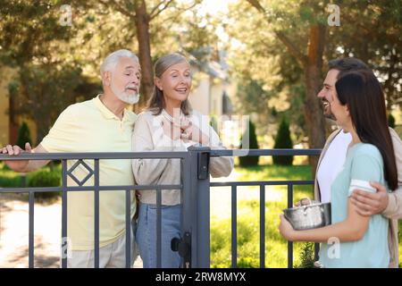 Rapporto amichevole con i vicini. Famiglia giovane che parla con coppie anziane vicino a recinzione all'aperto Foto Stock