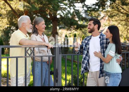 Rapporto amichevole con i vicini. Famiglia giovane che parla con coppie anziane vicino a recinzione all'aperto Foto Stock