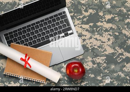 Notebook, diploma, laptop e mela su sfondo mimetico, base piatta con spazio per il testo. Educazione militare Foto Stock