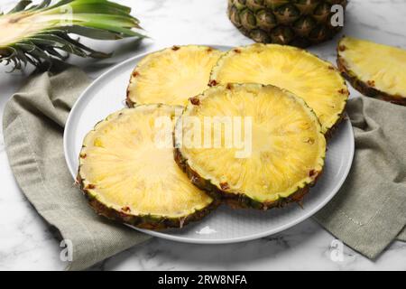 Fette di gustoso ananas maturo su un tavolo in marmo bianco, primo piano Foto Stock