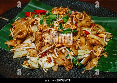 Tagliatelle di riso fritte o note come Kwetiau Goreng mescolate con alcune verdure sul piatto nero. Messa a fuoco selettiva. Foto Stock