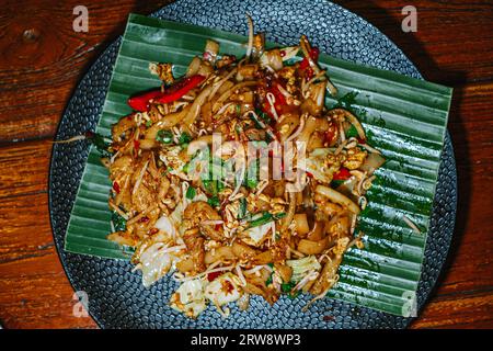 Piatto piatto o foto dall'alto di tagliatelle di riso fritte o conosciute come Kwetiau Goreng mescolate con alcune verdure sul piatto nero. Messa a fuoco selettiva. Foto Stock