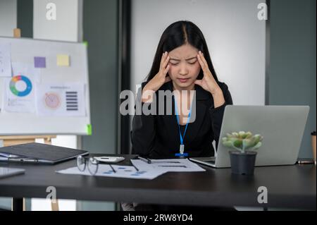 Una donna d'affari asiatica millenaria stressata e confusa o una lavoratrice finanziaria che lavora al suo progetto finanziario alla sua scrivania, pensando penosamente ad abo Foto Stock