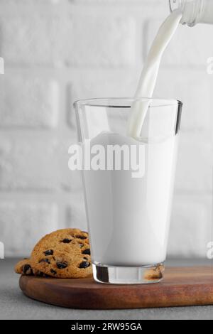 latte versato nel bicchiere dalla bottiglia e biscotti con gocce di cioccolato vicino Foto Stock