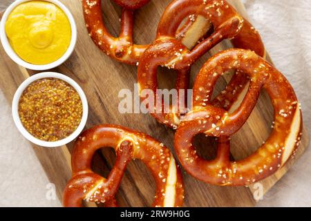 Morbidi Pretzel bavaresi fatti in casa con senape su un asse di legno, vista dall'alto. Foto Stock