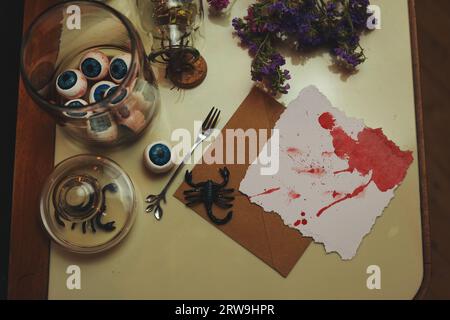 natura morta di halloween con una carta bianca e sanguinosa, palline oculari, scorpioni, insetti e fiori secchi Foto Stock