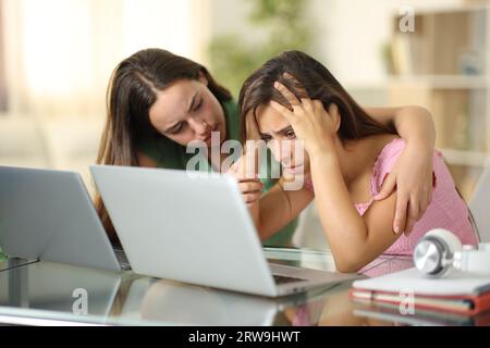 Triste studente che viene confortato da un altro che controlla il portatile a casa Foto Stock