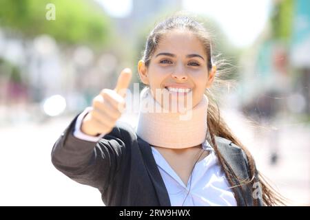 Ritratto frontale di una felice donna d'affari convalescente con i pollici in alto in strada Foto Stock