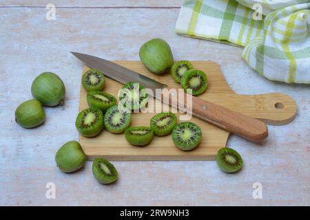 Mini kiwi, frutta intera e tagliata a metà su tavola di legno con coltello (Actinidia arguta) Foto Stock