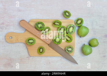 Mini kiwi, frutta intera e tagliata a metà su tavola di legno con coltello (Actinidia arguta) Foto Stock