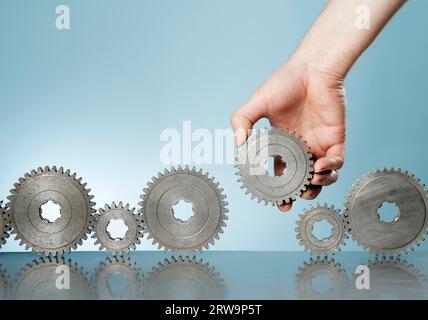 Uomo che aggiunge un ingranaggio dentato in una fila di vecchi ingranaggi dentati Foto Stock