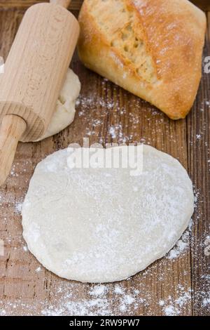 Stendere l'impasto lievitato su una tavola di legno. Dietro di esso un rotolo di impasto e un panino Foto Stock