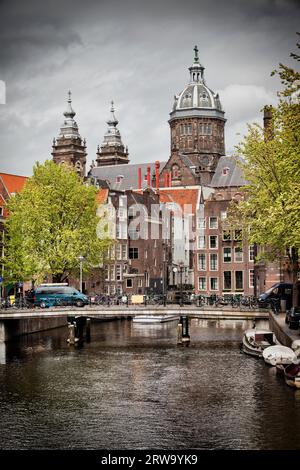 Città di Amsterdam nei Paesi Bassi, ponte, canale, edifici storici e torri della chiesa di San Nicola sullo sfondo Foto Stock