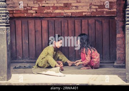 Bhaktapur, Nepal, circa giugno 2012: Due ragazze con lunghi capelli neri si siedono a terra all'aperto e giocano a Bhaktapur, Nepal. Documentario Foto Stock