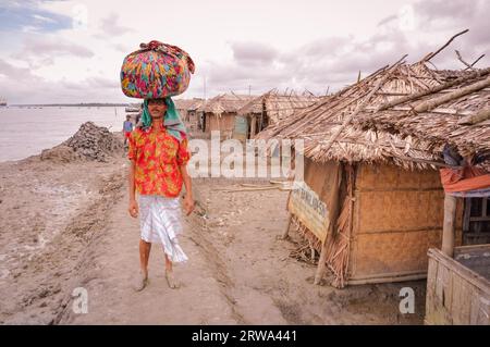 Sunderban, Bangladesh, circa luglio 2012: Uomo nativo con baffi si trova nel fango vicino a casa con carico pesante in stoffa colorata sulla testa a Sunderban Foto Stock