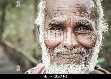 Sunderban, Bangladesh, circa luglio 2012: Vecchio nativo con barba e capelli bianchi indossa sciarpa colorata e camicia marrone e tiene in mano il bastone di legno Foto Stock