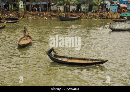 Dhaka, Bangladesh, circa luglio 2012: Foto di uomini nativi su barche sul fiume sullo sfondo con persone e case sulla riva a Dacca, Bangladesh. Foto Stock