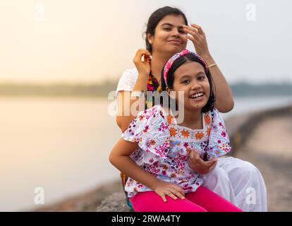 Madre e figlia indiane con un volto sorridente sedute sul fiume durante il tramonto Foto Stock